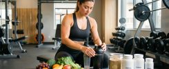 Une athlète assise sur un banc de musculation, entourée d’un shaker, d’aliments équilibrés et de contenants de compléments neutres.